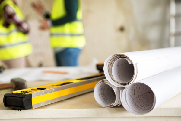 Rolled up builders plans on a table with two builders talking in the background